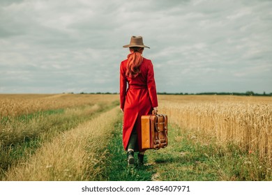 Stylish Woman with Red Hair in Vintage Red Coat with Suitcase Walking on Road Through Wheat Field, Freedom Concept - Powered by Shutterstock