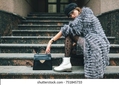 stylish woman in rich fur coat in city street, autumn fashion trend, black leather purse, cap, white boots, urban style, accessories, legs, footwear