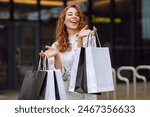 Stylish woman with shopping bags walks through the city streets. Consumerism, fashion, purchases, shopping, lifestyle concept. 