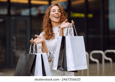 Stylish woman with shopping bags walks through the city streets. Consumerism, fashion, purchases, shopping, lifestyle concept. 