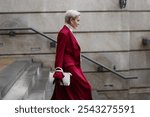 Stylish Woman with Short Haircut in Burgundy Coat Walks City Street, Wearing Fashionable clothing White Turtleneck Sweater, White Bag. Confident and Chic Mature Fashion Model