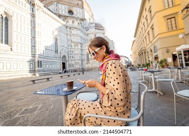 Stylish woman sitting with phone on cafe terrace near famous Duomo cathedral in Florence during morning time. Concept of italian lifestyle and travel Italy