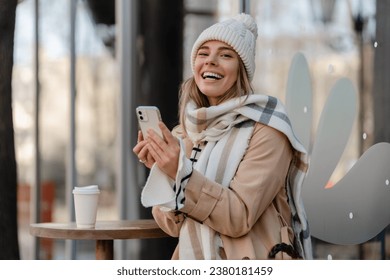 stylish woman walking in winter street wearing beige coat, knitted hat, scarf, smiling happy cold season fashion trend, using smartphone - Powered by Shutterstock