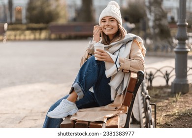 stylish woman walking in winter street wearing beige coat, knitted hat, scarf, smiling happy cold season fashion trend, drinking coffee - Powered by Shutterstock