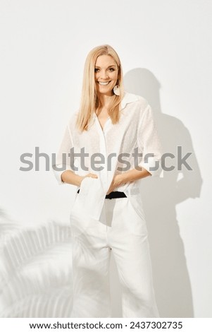 Stylish woman in a white outfit is captured mid-pose. The dramatic interplay of light and shadow accentuates her elegance and casts an artistic silhouette against a white background.