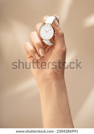 Stylish women's watch on a woman's hand. Woman's hand holding a gold white watch on a beautiful beige background. Concept for watch shops
