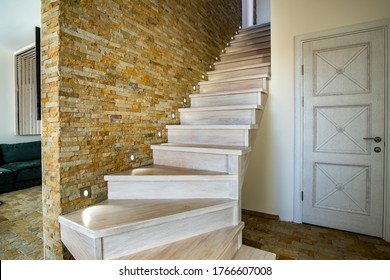 Stylish wooden contemporary staircase inside loft house interior. Modern hallway with decorative limestone brick walls and white oak stairs.