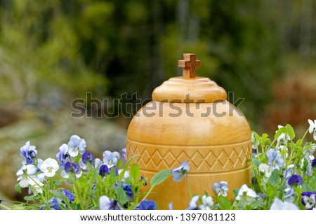 stylish wooden funerary urn standing in nature among blue and white violets ready for spreading of the ashes