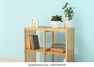 Stylish wooden shelving unit with houseplants and books near blue wall in room - Shutterstock ID 2341549169