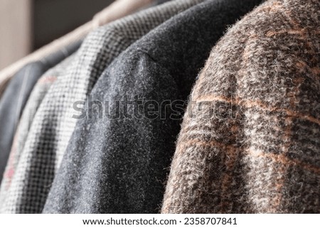 Stylish wool jackets of different colors hang on hangers. Row of men suit jackets on hangers. Shallow depth of field