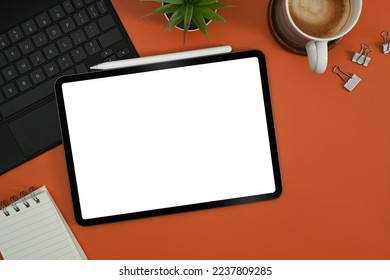 Stylish work table with digital tablet, notepad, coffee cup and potted plant on orange background - Powered by Shutterstock