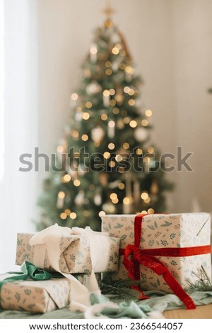 Stylish wrapped christmas gifts with ribbon on table on background of decorated christmas tree, rustic fireplace and festive lights. Merry Christmas! Atmospheric winter holidays