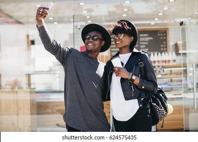 Stylish young african couple in sunglasses drinking coffee and making selfie a street of summer