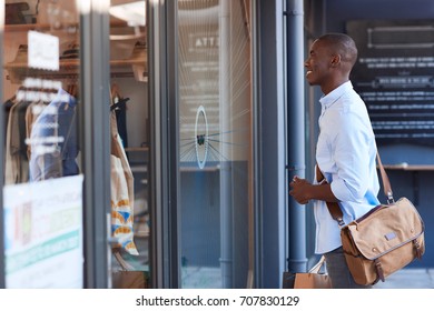 Stylish Young African Man Carrying Shopping Bags And Looking At A Clothing Store Window Display While Out Shopping In The City