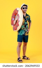 Stylish Young Asian Man With Sunglasses Holds Colorful Swim Ring. Half Body Studio Portrait On Yellow Background. Summer Vacations Start Concept