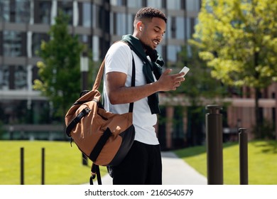 Stylish Young Black Man In Wireless Headphones Using Cell Phone Walking Down The Street In The Urban City. Cheerful Trendy Guy Listening To Favorite Music Spending Time Outdoors, Walking Resting Alone - Shutterstock ID 2160540579