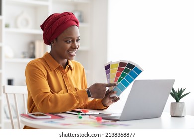 Stylish Young Black Woman In Red Turban Independent Contractor Having Video Conference With Client, Female Designer Sitting At Workdesk In Front Of Laptop At Home, Showing Color Palette, Copy Space