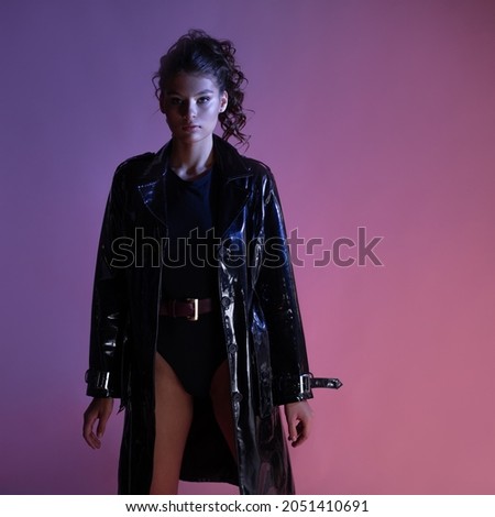A stylish young brunette in a latex raincoat over a black bodysuit, a noir fashion image in a mysterious blurred silhouette goes into the shadows