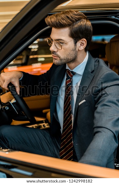 stylish young businessman closing door while\
sitting in automobile