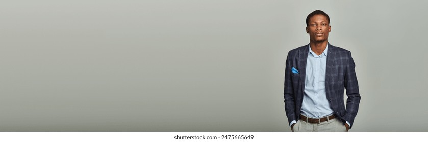 A stylish young businessman in formal checkered blazer confidently poses in front of a plain gray background.