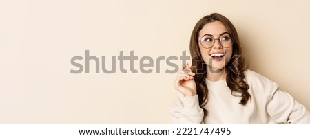 Stylish young caucasian woman wearing glasses and smiling, posing against beige background. Copy space