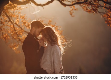 Stylish young couple in the autumn mountains. A guy and a girl hug together under a large old tree on a background of a forest and mountain peaks at sunset.