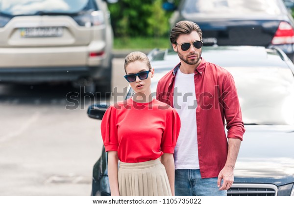 stylish young couple of models in sunglasses posing near\
car 