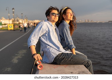 Stylish young couple sitting on concrete pier at seaside enjoy sunset. Happy man and woman in casual street style clothes and trendy sunglasses relaxed looking at river or sea in setting sunlight - Powered by Shutterstock