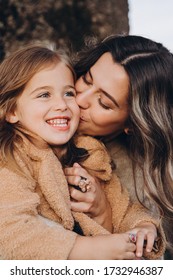 Stylish Young Family In The Autumn Mountains. Mom And Daughter Are Sitting Under A Large Old Tree And Hugging Against The Background Of The Forest And Mountain Peaks At Sunset.