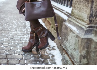 Stylish young fashionable woman with dark brown leather bag and high heel winter boots. Winter street fashion look