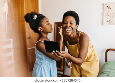 Stylish young girl applying makeup on her mother's beautiful face, using a makeup palette for the beauty routine to find the perfect foundation shade. Little girl styling her mom with confidence. - Powered by Shutterstock