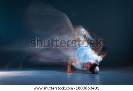 Stylish young guy breakdancer dancing hip-hop on the floor in neon light. Dance school poster. Long exposure shot