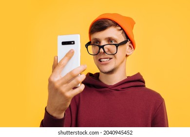 Stylish Young Guy In An Orange Hat With Glasses And A Red Sweater Unlocked The Phone With His Eyes, Biometrics For The Eyes, Secure Entry Into Phone