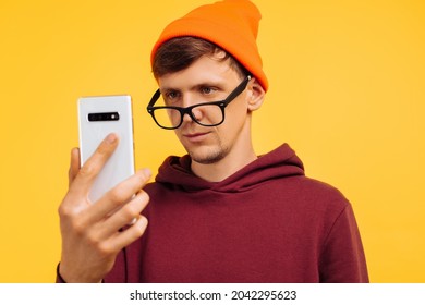 Stylish Young Guy In An Orange Hat With Glasses And A Red Sweater Unlocked The Phone With His Eyes, Biometrics For The Eyes, Secure Entry Into Phone