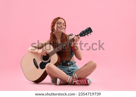 Stylish young hippie woman playing guitar on pink background