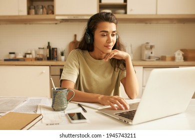 Stylish Young Latin Woman Interpreter Translating Video Conference Via Online Chat, Wearing Wireless Headset, Sitting At Home In Front Of Open Laptop. Electronic Gadgets And Communication Concept