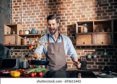 Stylish Young Man With Apron Frying Vegetables