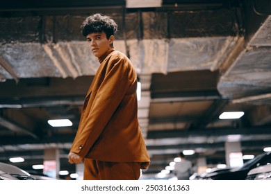 Stylish young man in a brown suit, standing confidently in an underground parking garage with modern cars around - Powered by Shutterstock