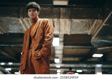 Stylish young man in a brown suit standing confidently in an industrial setting with metallic surfaces and soft lighting - Powered by Shutterstock