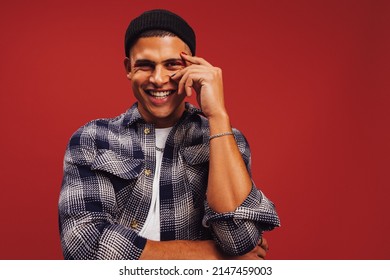 Stylish young man smiling cheerfully in a studio. Happy young man standing alone against a red background. Fashionable young man wearing nail polish and eye shadow. - Shutterstock ID 2147459003