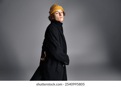 A stylish young man stands confidently in a black coat and yellow beanie, exuding urban flair in a studio. - Powered by Shutterstock