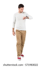 Stylish Young Man Walking And Checking Time On Wrist Watch. Full Body Length Portrait Isolated Over White Studio Background. 