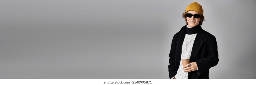 A stylish young man with a warm smile sips coffee in a sleek studio, wearing a black coat and yellow beanie. - Powered by Shutterstock