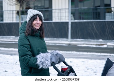 Stylish Young Mom With A Cup Of Coffee On A Walk With A Baby Carriage In Winter.