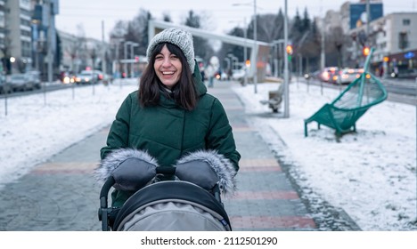 Stylish Young Mother For A Walk With Her Baby In A Baby Carriage In Winter.