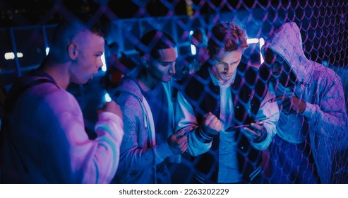 Stylish Young Multiethnic Men Watching a Sports Game on Smartphone, Supporting Their Favorite Team. Celebrating Goal, Betting or Lottery Win. Standing Outside in Urban Spot with Neon Lights at Night - Powered by Shutterstock