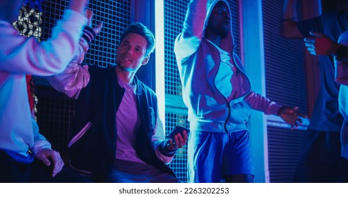 Stylish Young Multiethnic Men Watching a Sports Game on Smartphone, Supporting Their Favorite Team. Celebrating Goal, Betting or Lottery Win. Standing Outside in Urban Location with Neon Lights - Powered by Shutterstock