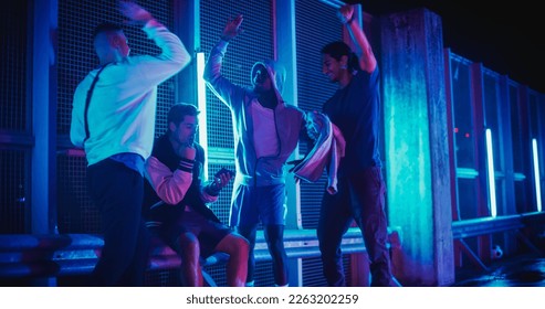 Stylish Young Multiethnic Men Watching a Sports Game on Smartphone, Supporting Their Favorite Team. Celebrating Goal, Betting or Lottery Win. Standing Outside in Urban Location with Neon Lights - Powered by Shutterstock