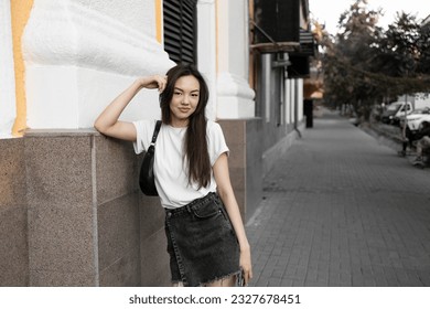 Stylish young pretty long hair brunette woman wearing white t-shirt, dark short jeans skirt and white modern sneakers having fun on the summer city street - Powered by Shutterstock