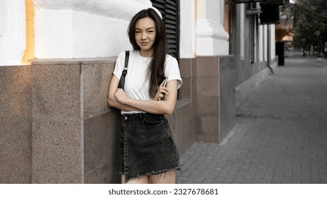 Stylish young pretty long hair brunette woman wearing white t-shirt, dark short jeans skirt and white modern sneakers having fun on the summer city street - Powered by Shutterstock